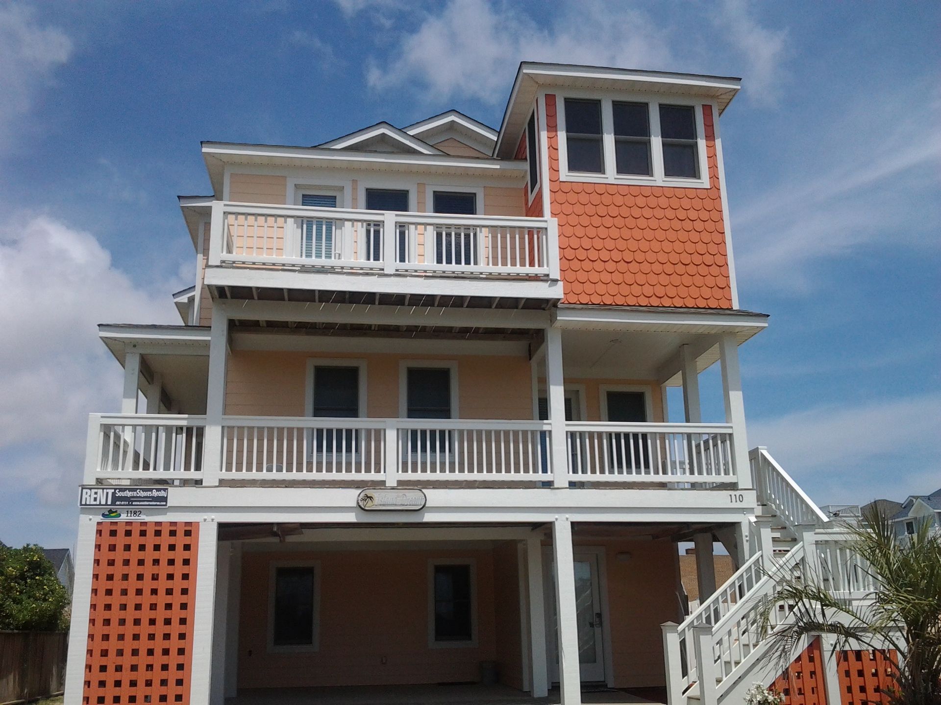 Two-story beach house, peach and orange exterior, balconies, staircases, sunny day.