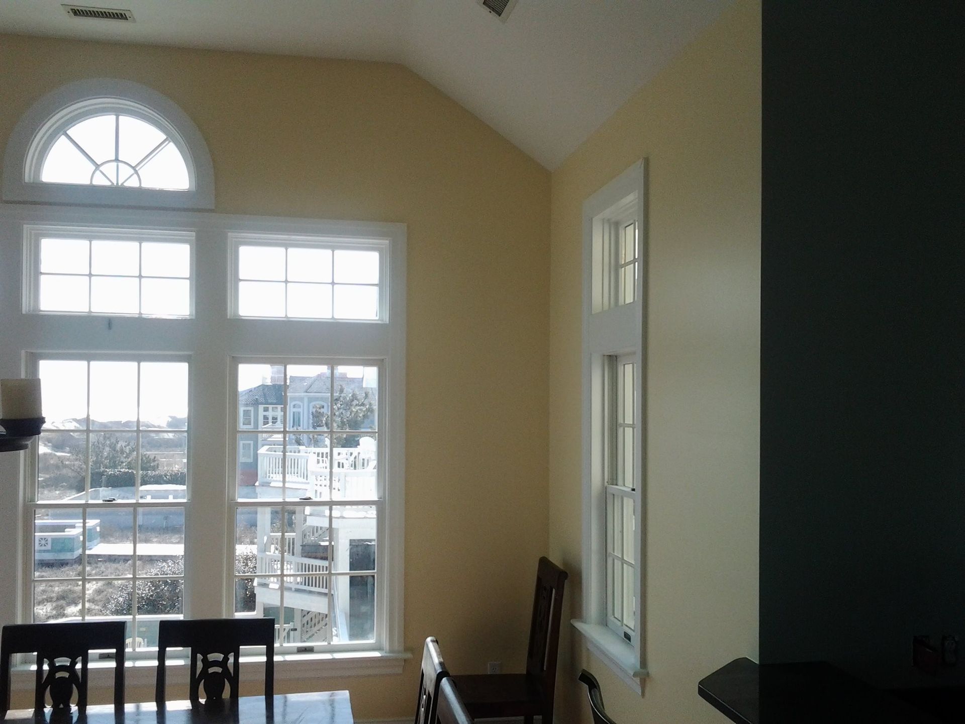 Large windows in a room with yellow walls and a high ceiling. Table and chairs in foreground.