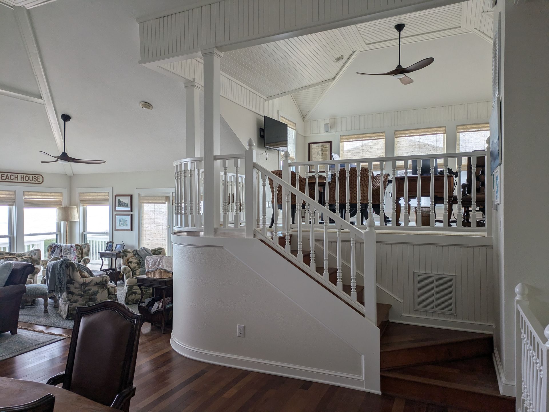 Interior with white railing staircase, open to living area with high ceiling, windows.