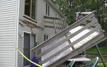 Damaged house deck, partially detached from siding. Yellow caution tape present.