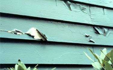Peeling blue paint on horizontal siding; sunlight visible.