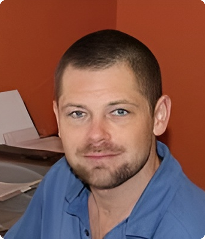 Man with short brown hair and a goatee, wearing a blue shirt, smiling in front of an orange wall.
