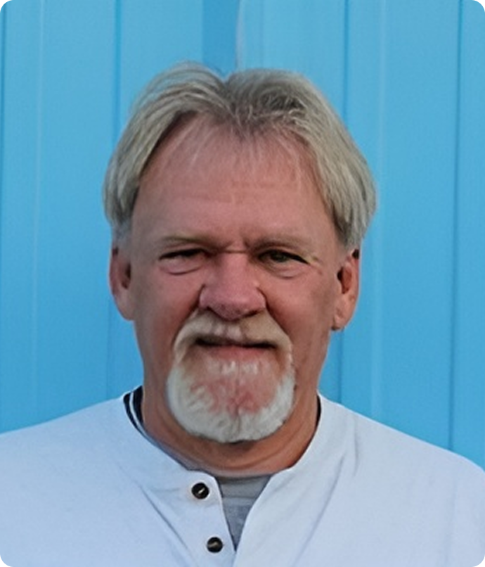 Man with graying hair and beard in front of a blue background, wearing a white shirt.