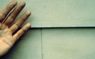 Hand with dusty fingers next to light-colored, horizontal wall siding.