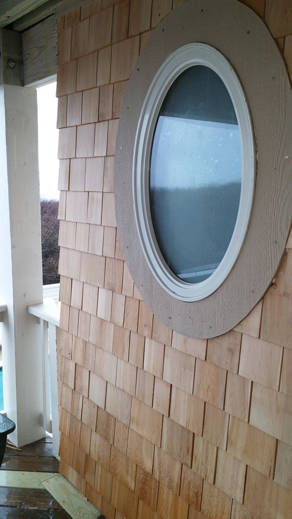 Oval window with white frame and wooden shingle siding on a building's exterior.