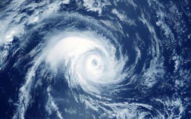 Overhead view of a hurricane swirling over a deep blue ocean, white clouds form a spiral.