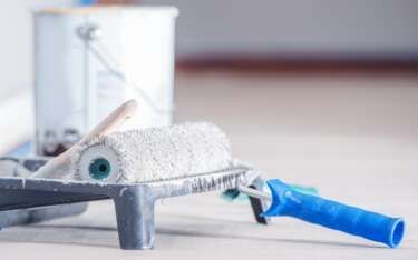 Paint roller and tray with a paint can in the background; preparing to paint.