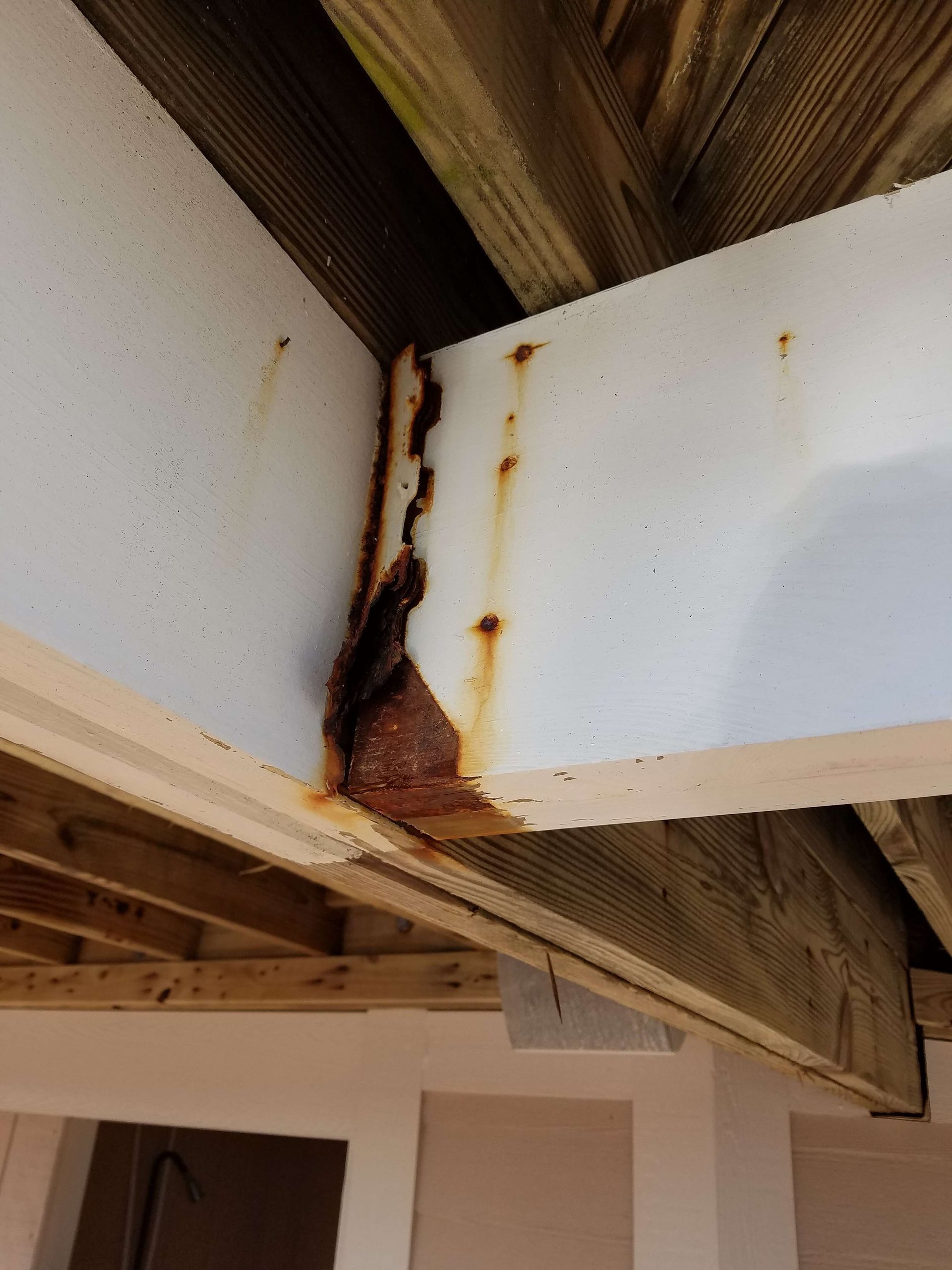 Severely rusted white metal beam supporting a deck, with wood framing above.