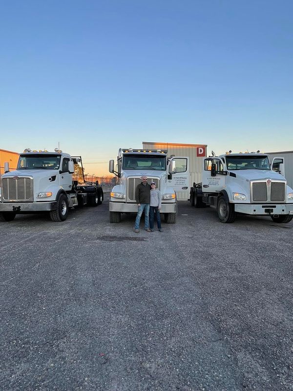 Three white semi-trucks with two people standing between the middle truck, blue sky backdrop.