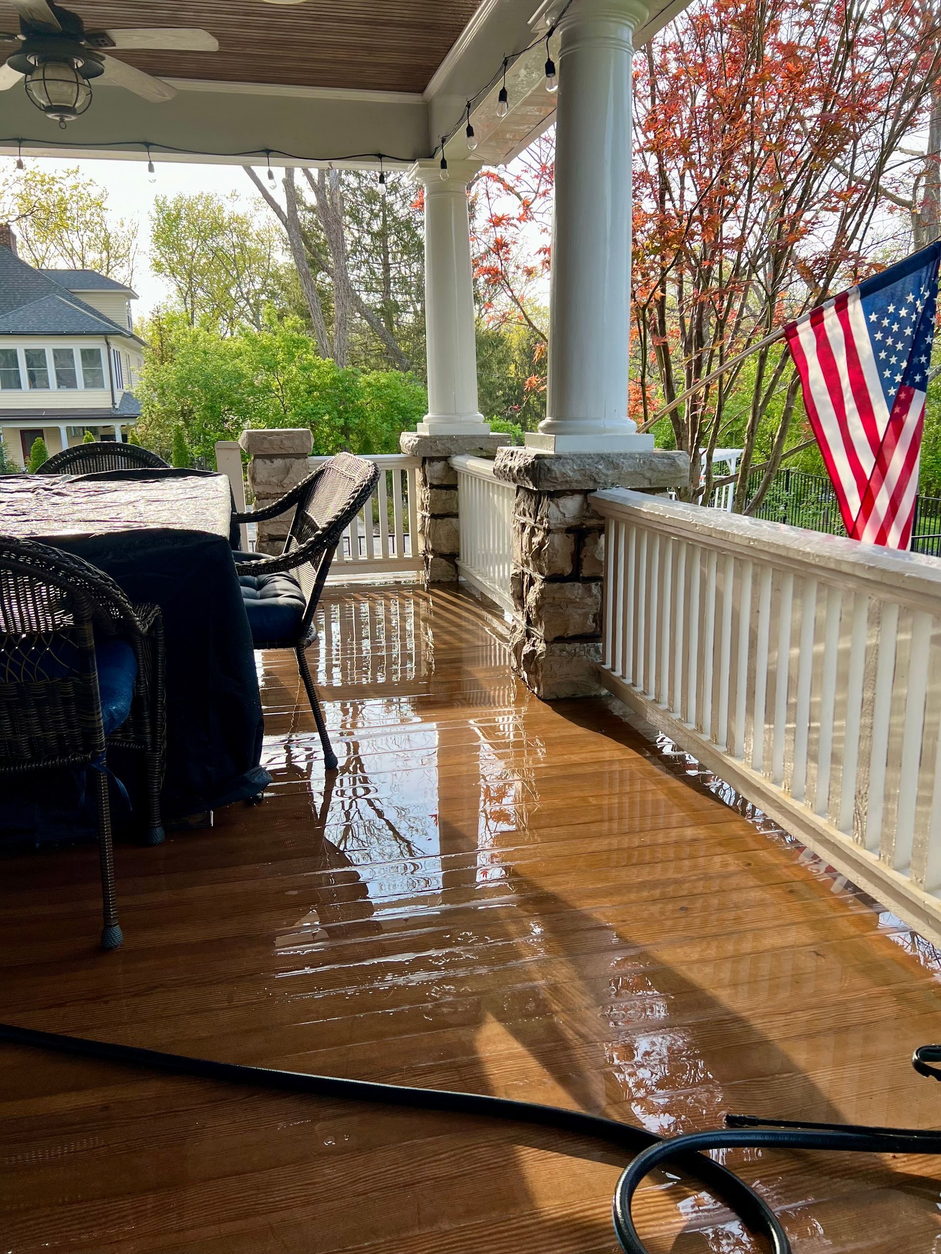 A flooded wooden porch with chairs, columns, and an American flag hanging from the white railing.