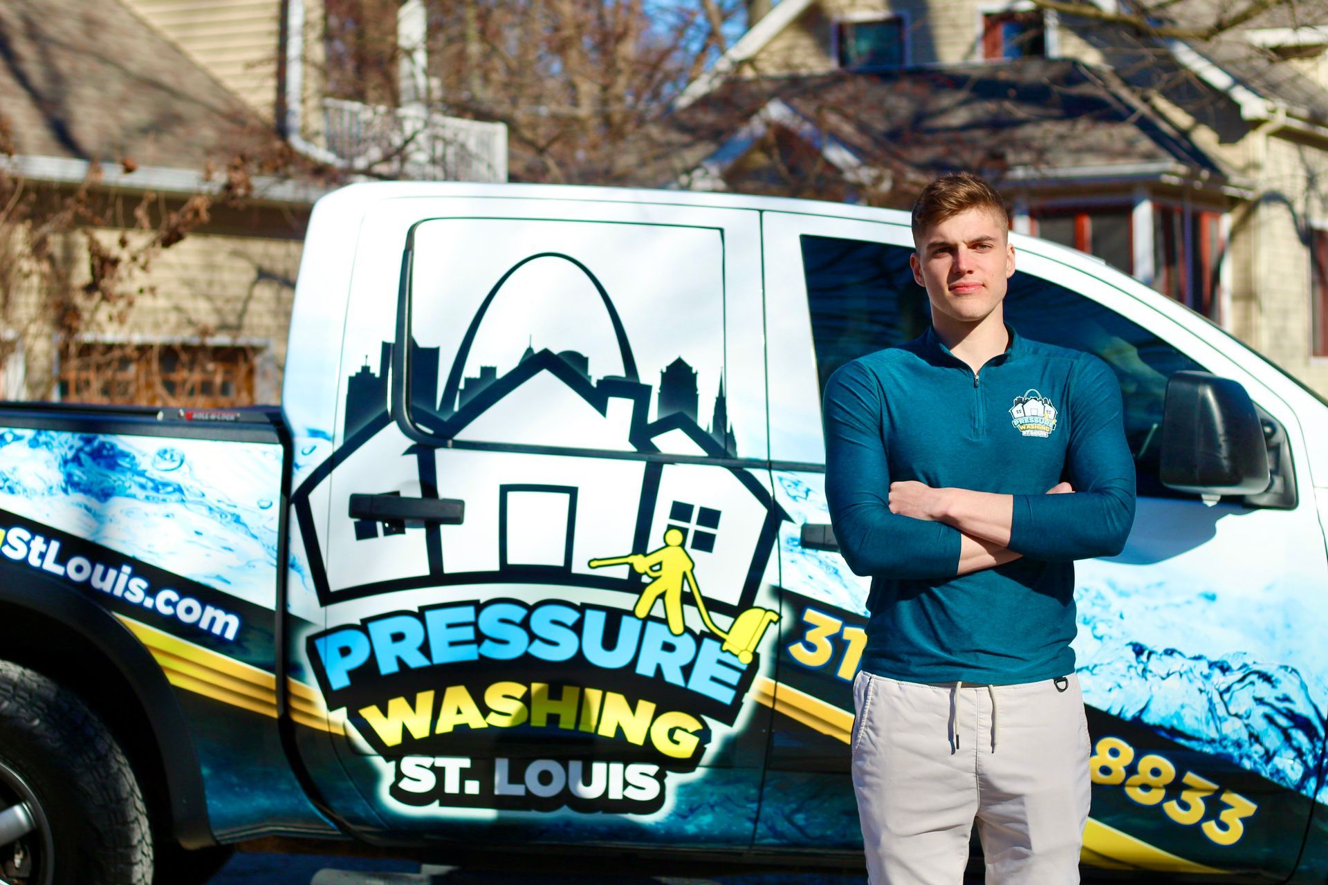 A person standing with arms crossed in front of a white truck branded with a St. Louis pressure washing business logo.