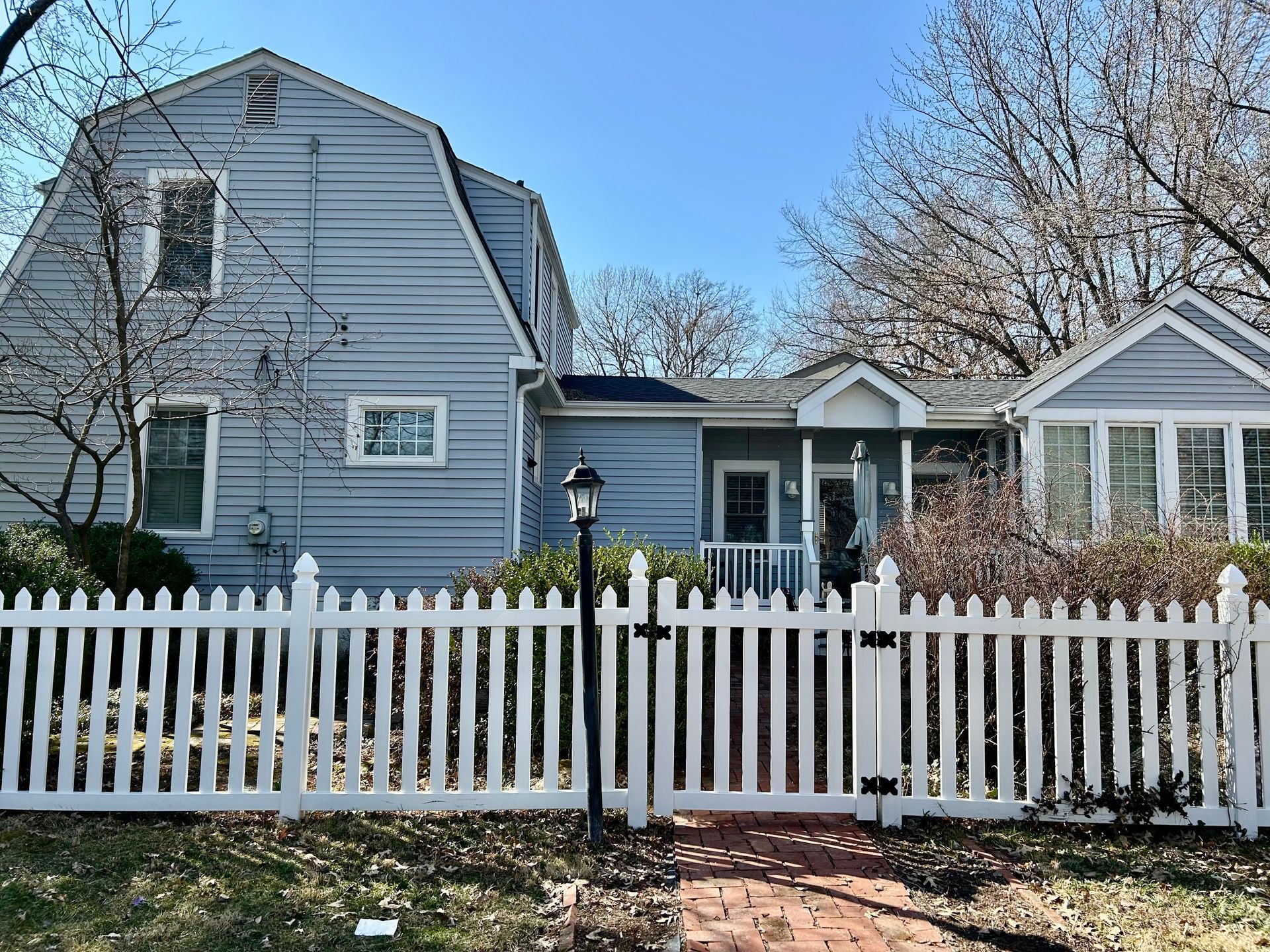 A blue, two-story house with a gambrel roof and a white picket fence on a sunny day.