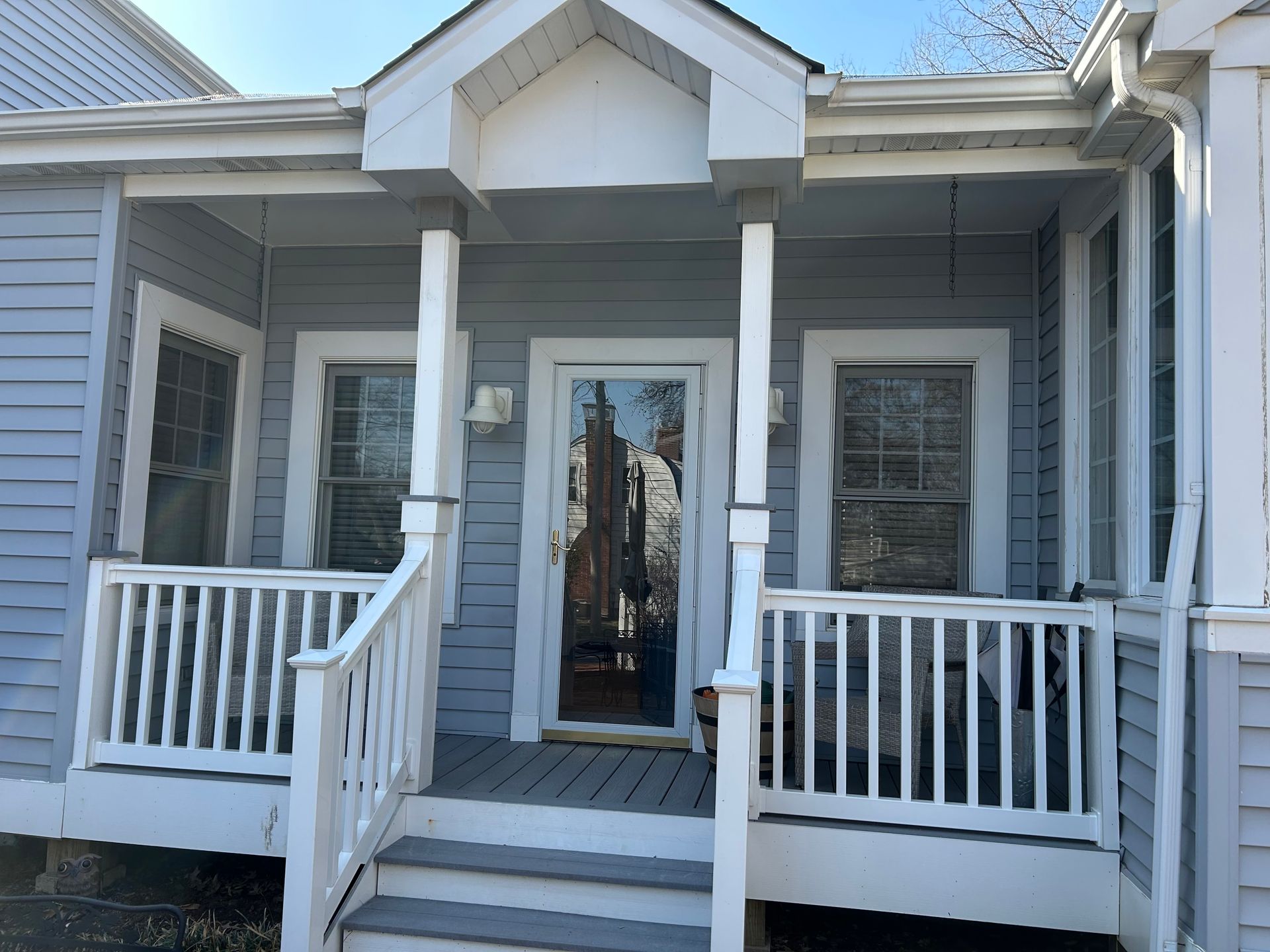 A porch with light blue siding, white railings, a glass storm door, and stairs leading to a small covered entryway.