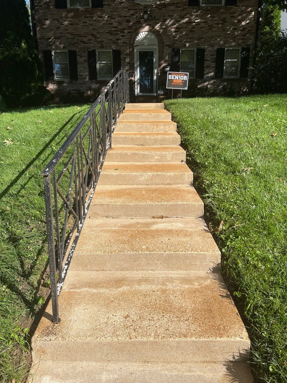 Concrete steps with a decorative metal handrail leading up to the front entrance of a brick house.
