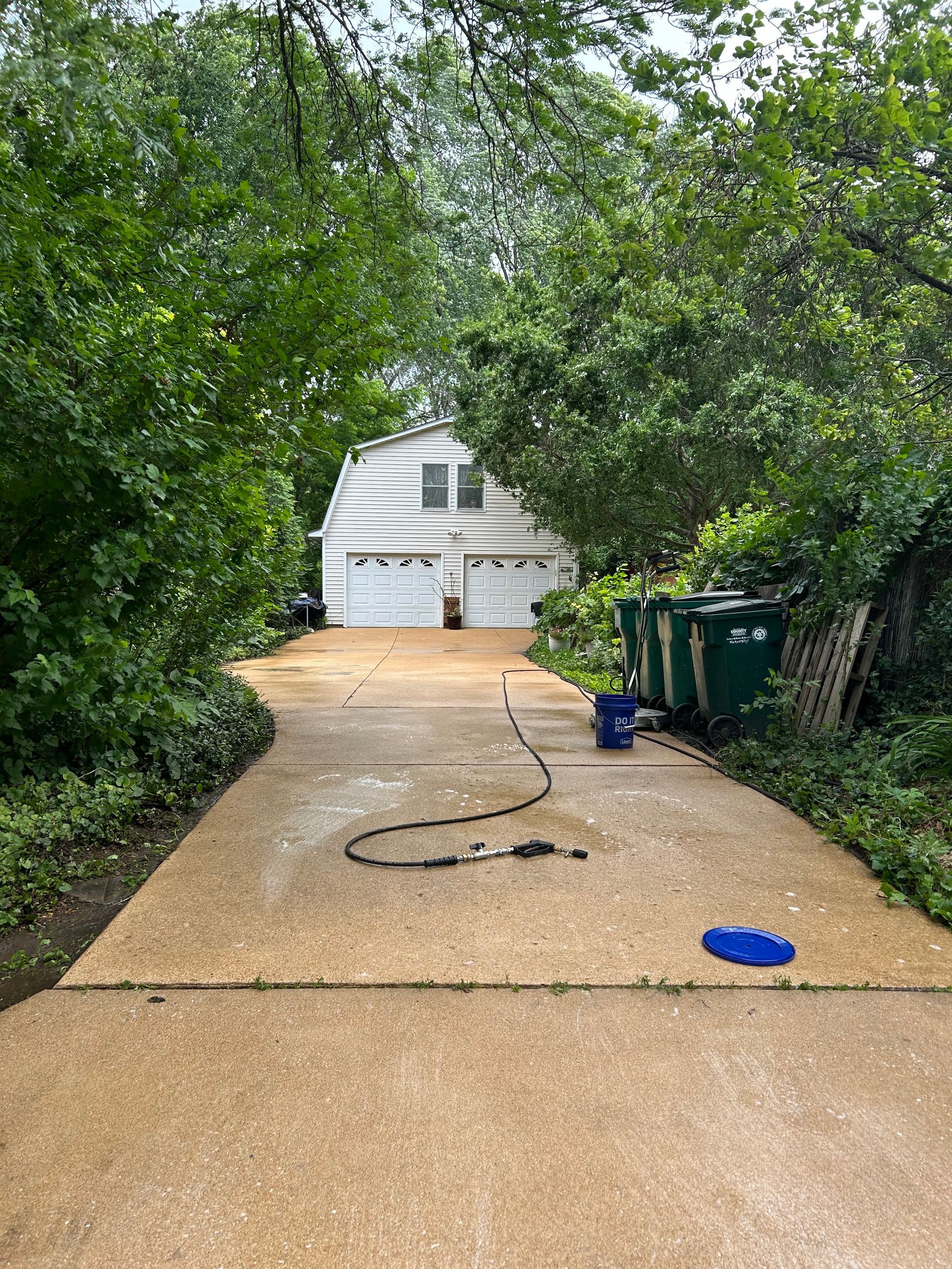 A tan concrete driveway framed by green trees leads to a detached white two-car garage with black trim.