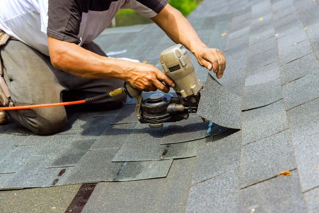 Worker cutting roof shingles with a power saw on a shingled roof
