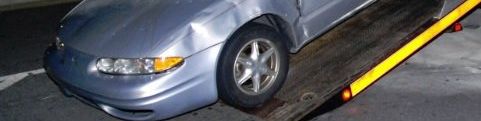 A silver car is being towed by a tow truck.