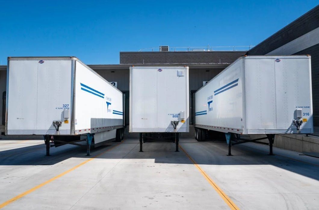 A row of white semi trucks are parked in a parking lot.