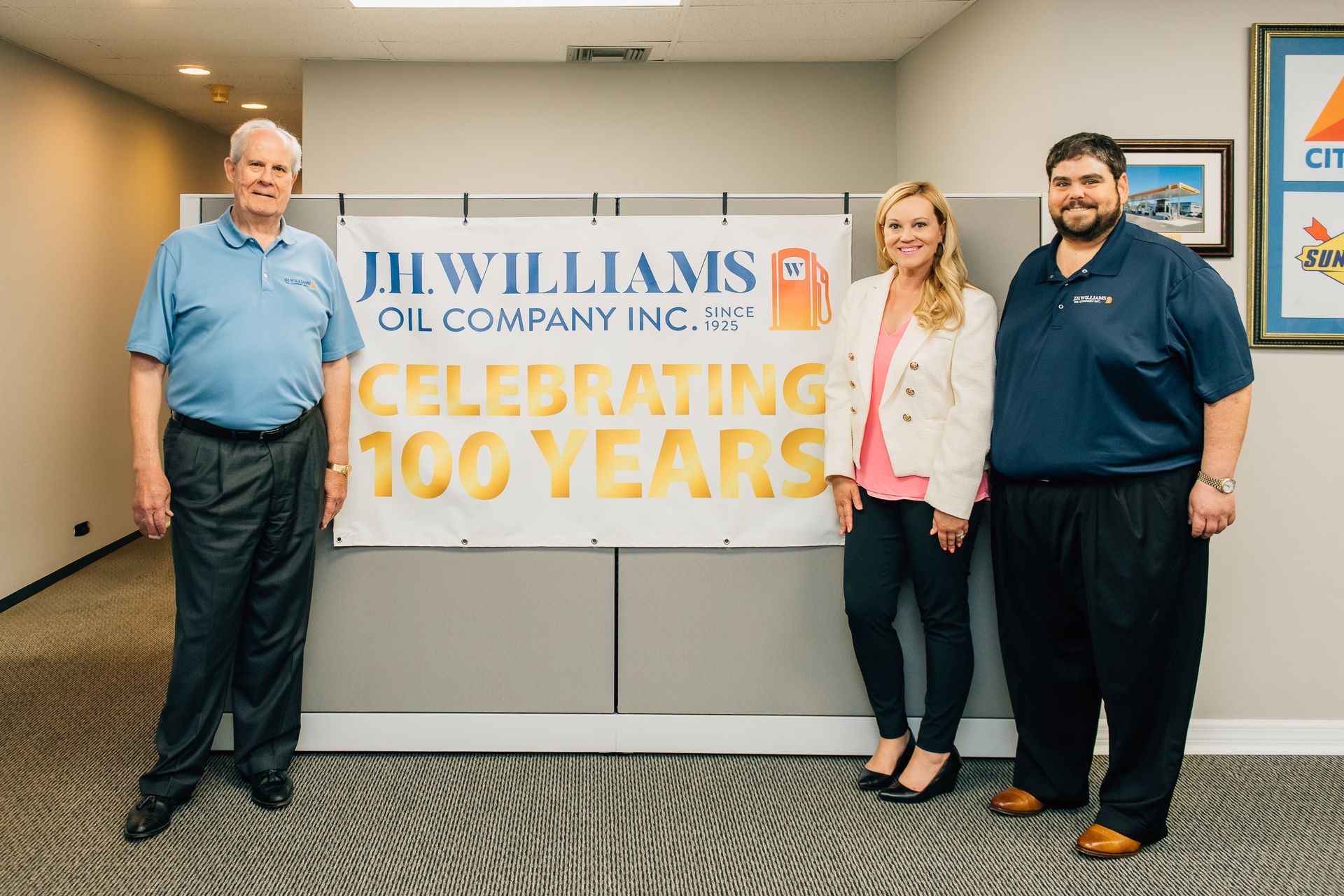 Three people are standing in front of a sign that says celebrating 100 years.