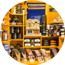 Wooden shelves filled with men's grooming products, belts, and a decorative house, lit shop display.
