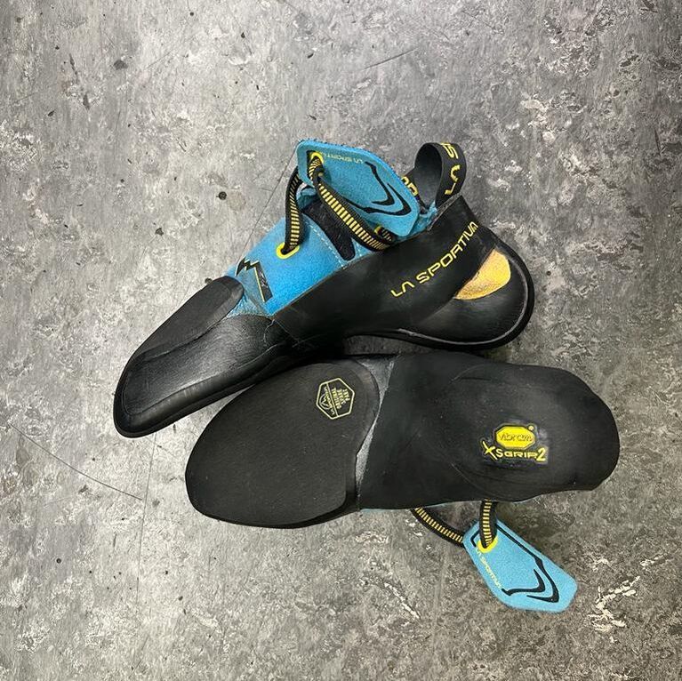 Pair of black and blue La Sportiva climbing shoes on a gray surface. One shoe is upside down, showing its sole.