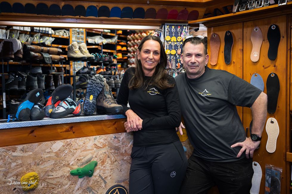 Two people, a woman and a man, standing in a shop, both wearing branded shirts, smiling.