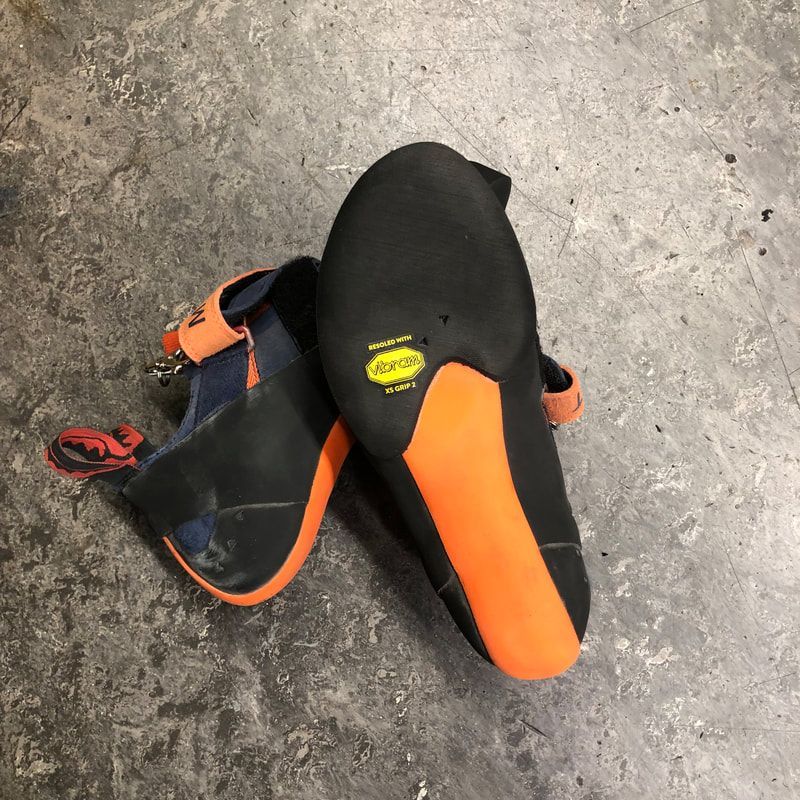 Climbing shoes, black uppers, orange accents and soles, lying on a gray surface.