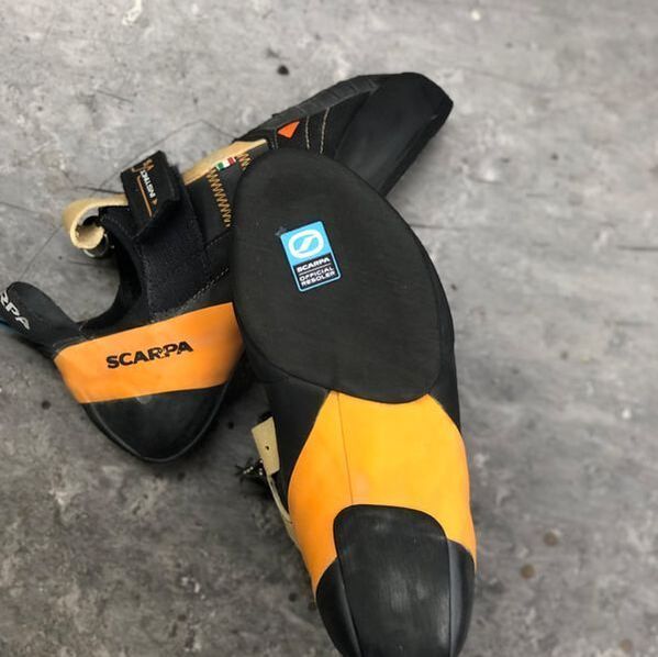 Pair of black and yellow Scarpa climbing shoes on a concrete surface.