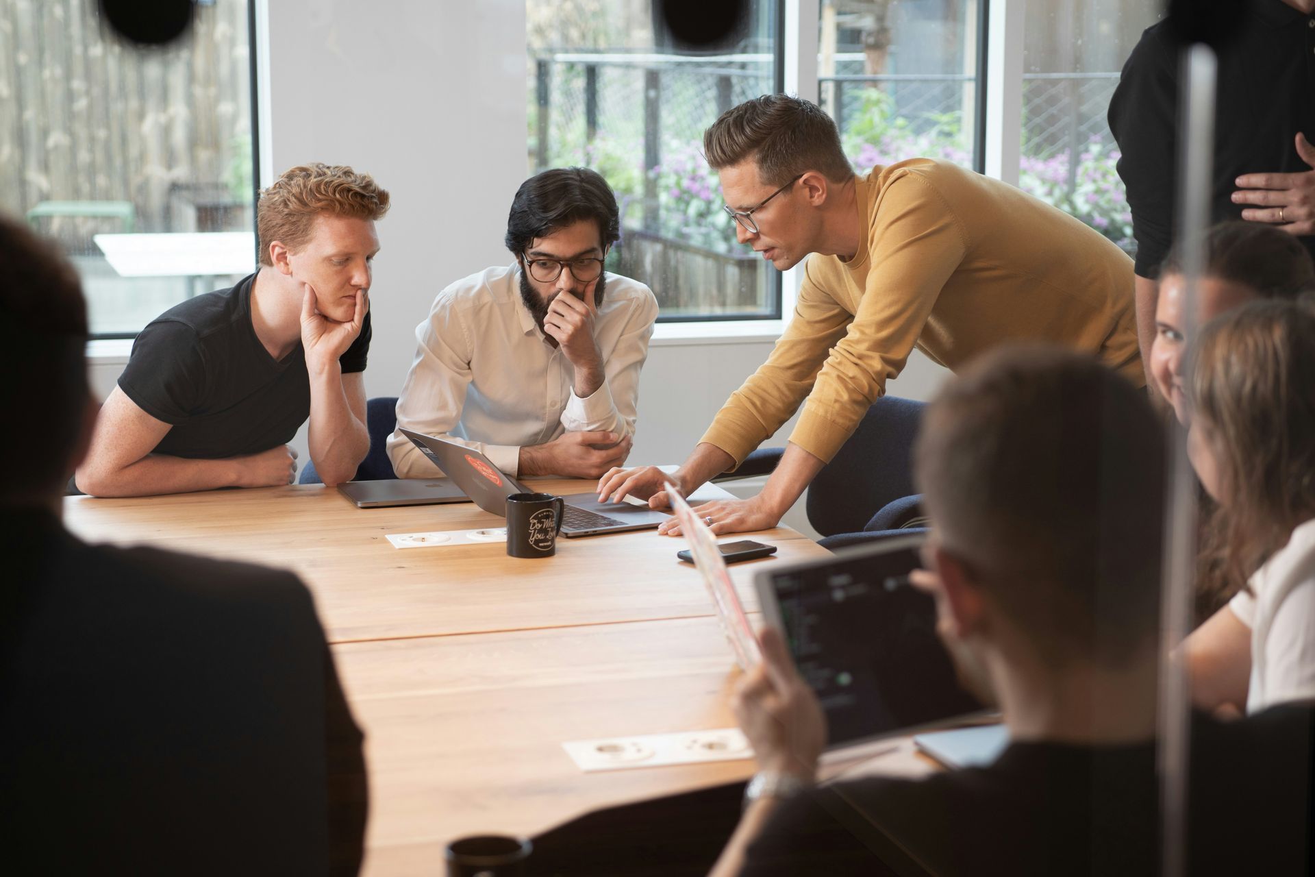 People gathered at a table, looking at laptops and discussing a project in an office.