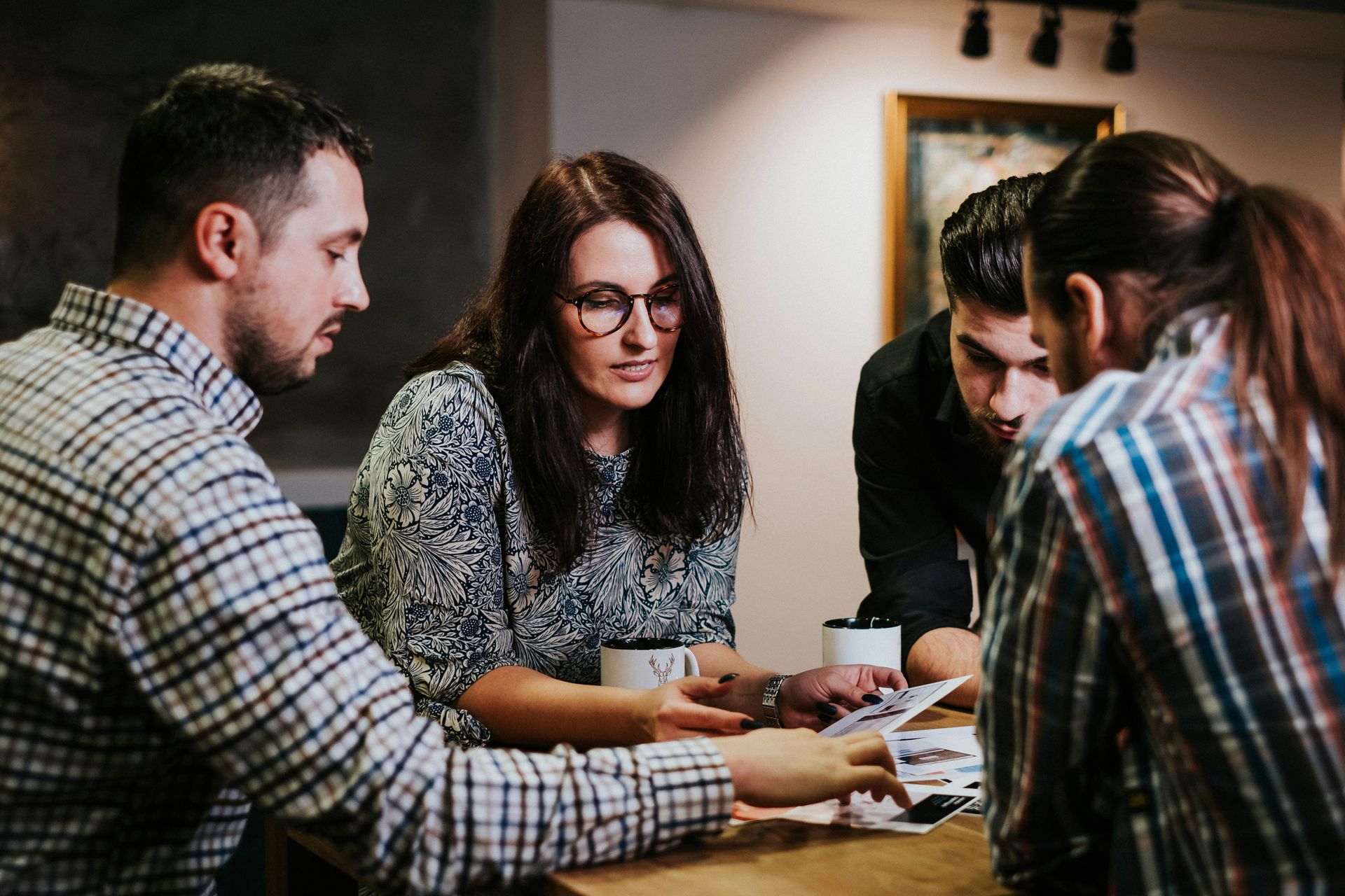 Four people review papers around a table in a warm-lit space; focused expressions.