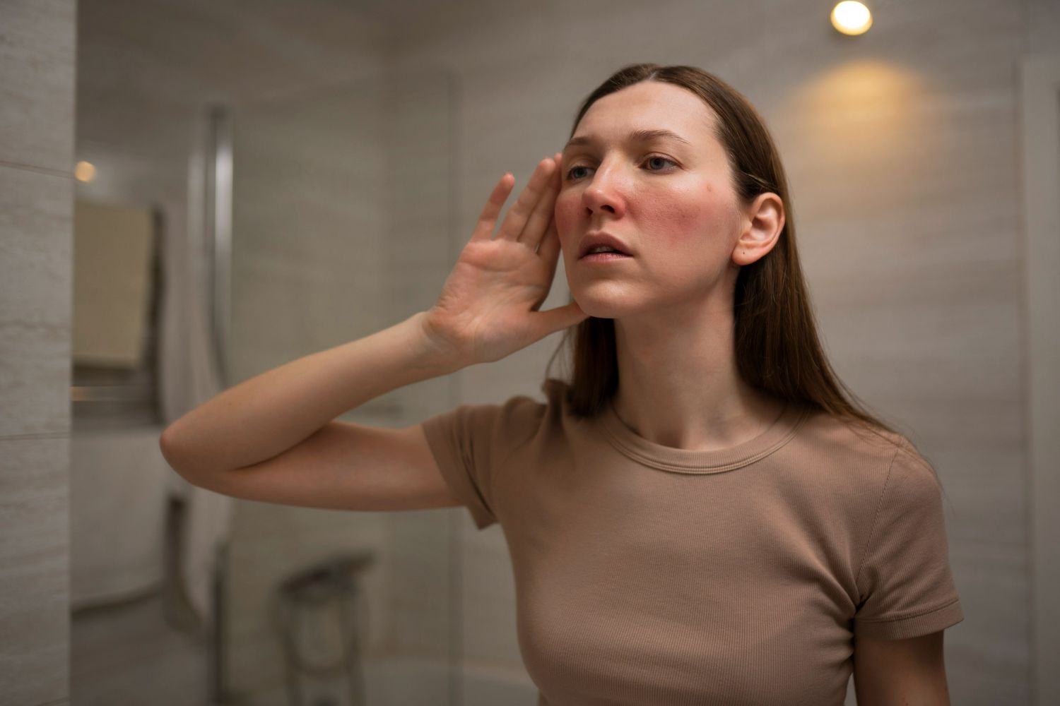 Woman looks at her reflection in a mirror; she has redness on her face.