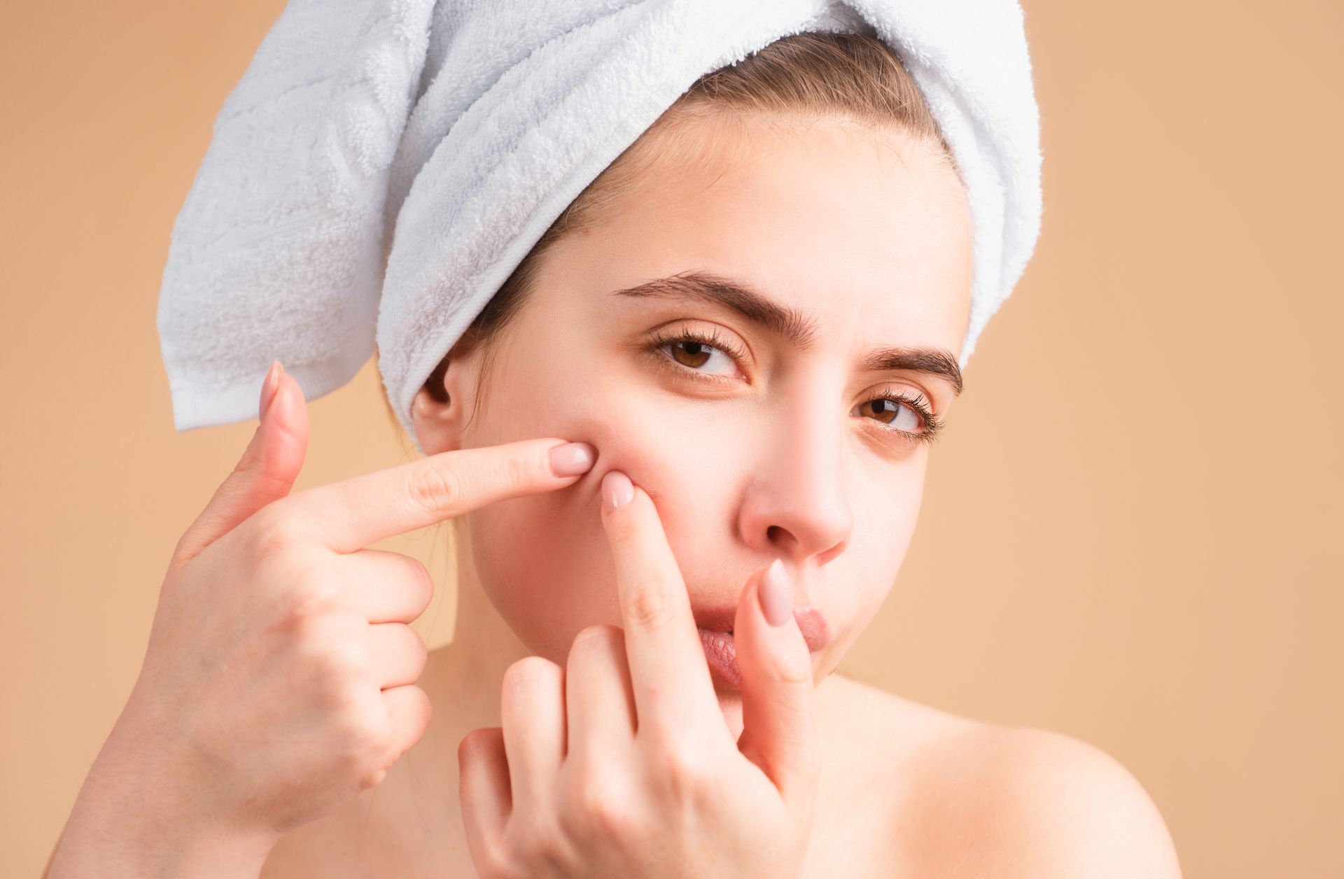 A woman with a towel wrapped around her head is scratching her face.