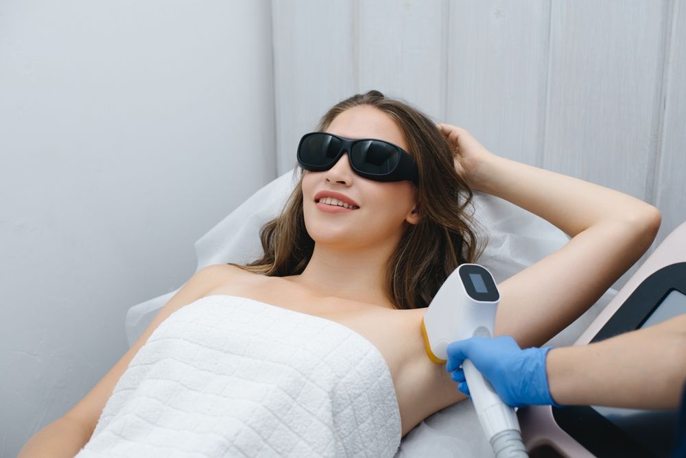 Woman getting laser hair removal on her underarm. She wears protective glasses and smiles.
