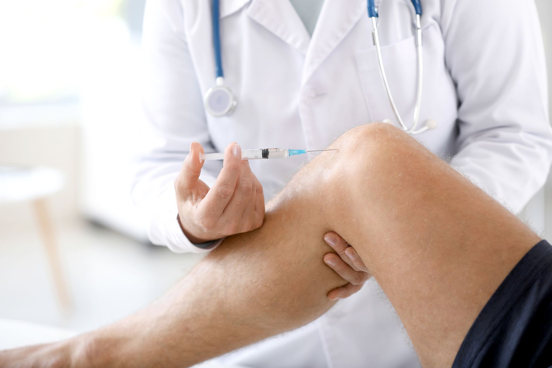 Doctor injecting medicine into a patient's knee in a medical setting. The doctor wears a white coat and uses a syringe.