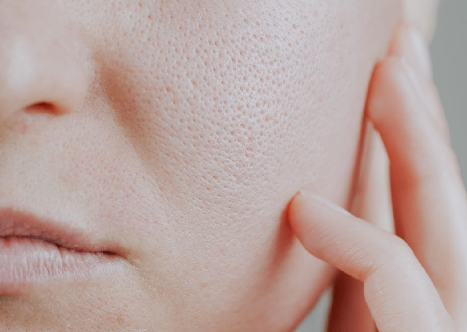 Close-up of a person's face showing enlarged pores on the cheek, with a hand touching the skin.