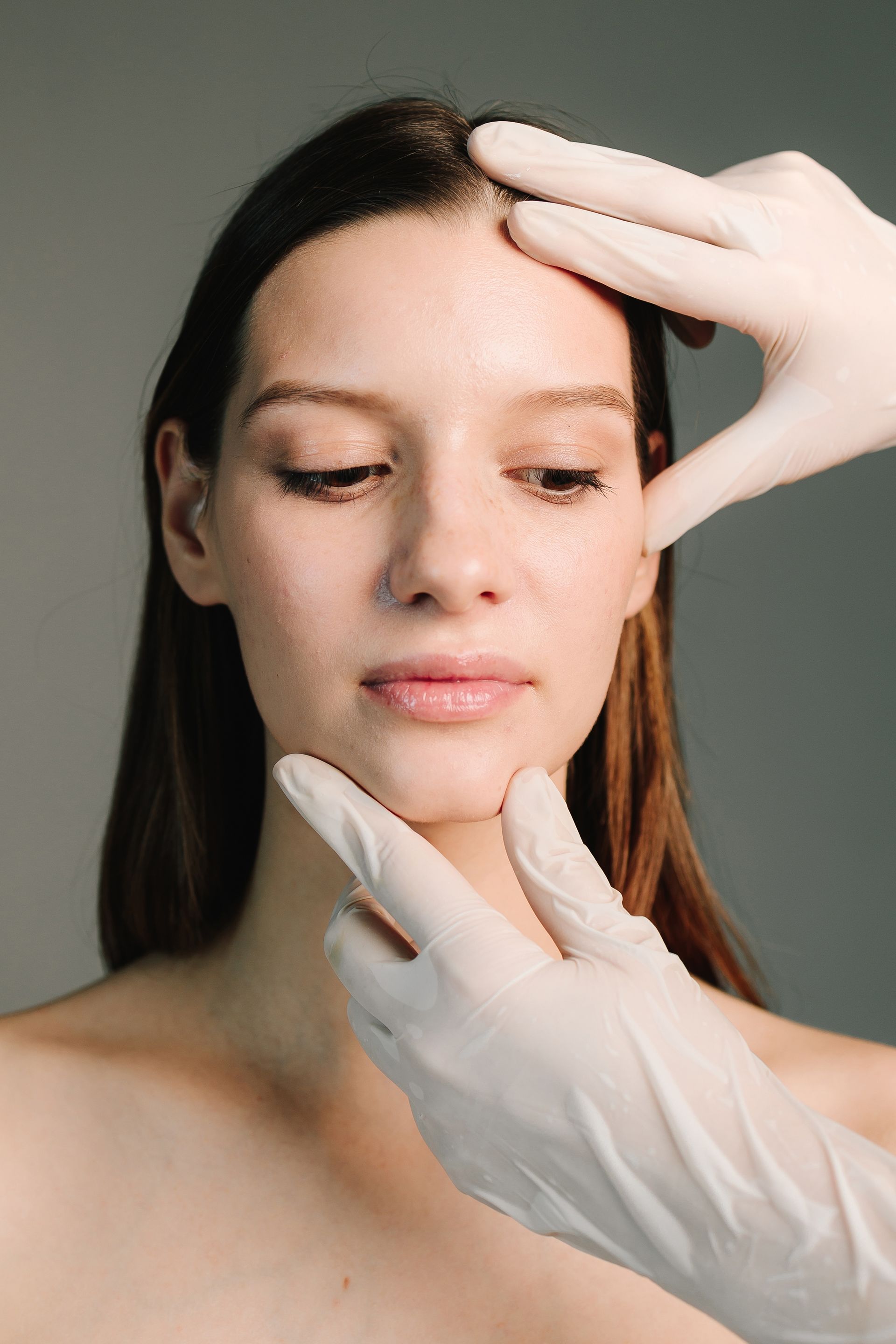 A woman's face being examined by gloved hands, in a medical setting.