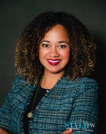 Woman with curly brown hair wearing a blue tweed blazer, smiling with dark lipstick.