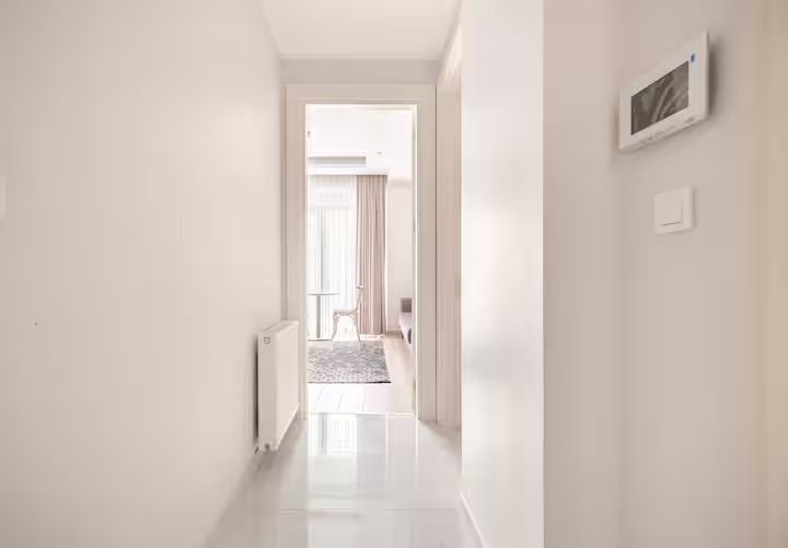 A hallway with white walls and a white floor leading to a bedroom.
