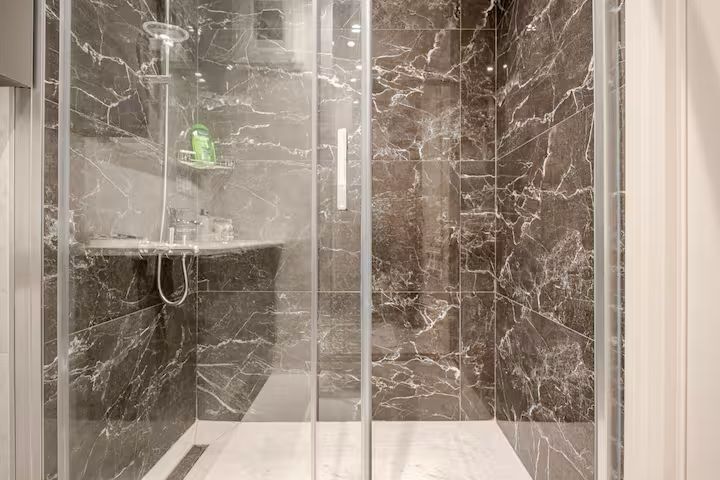 A bathroom with marble walls and a walk in shower with a glass door.