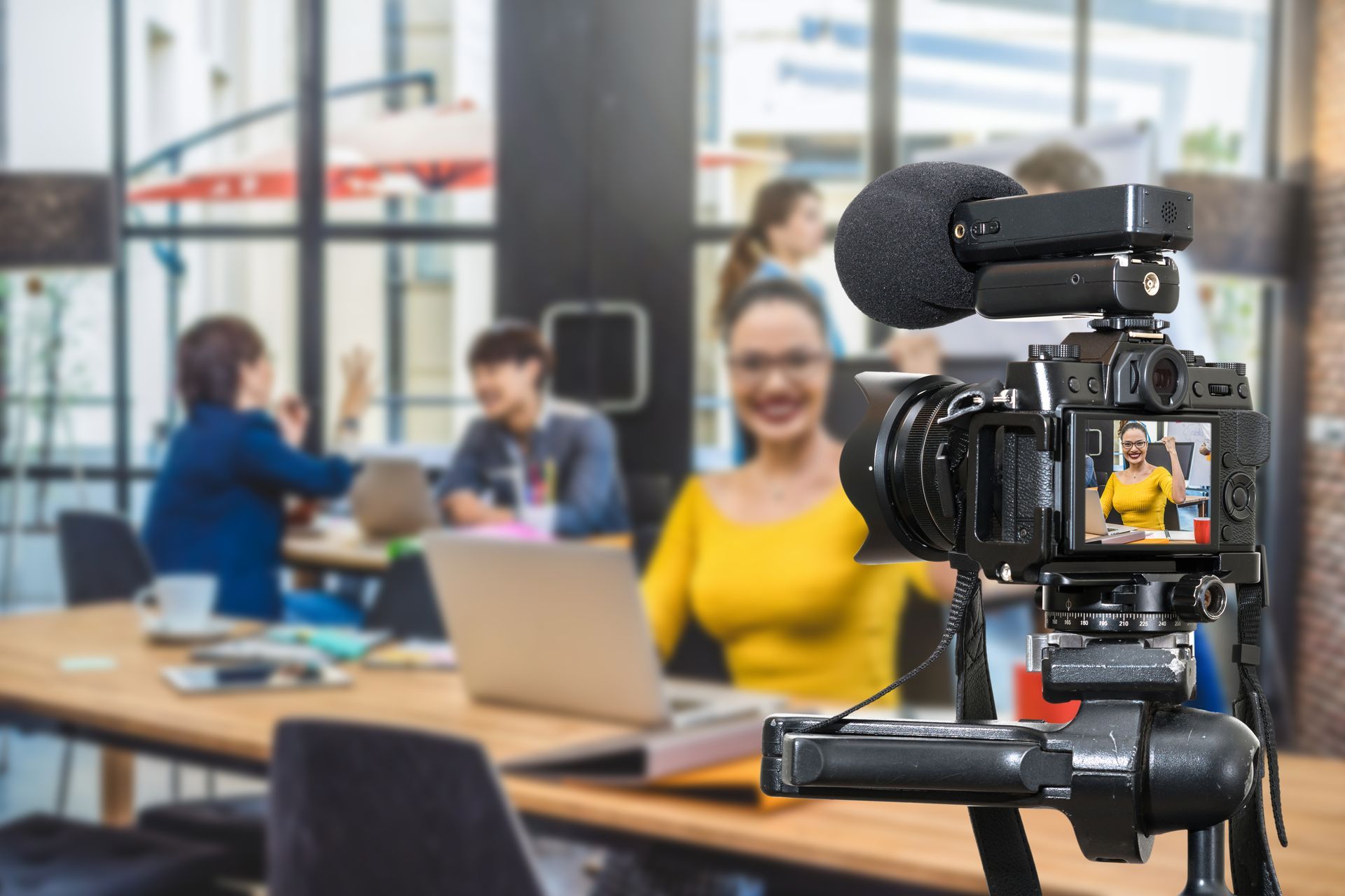 A video camera is recording a woman sitting at a table with a laptop.