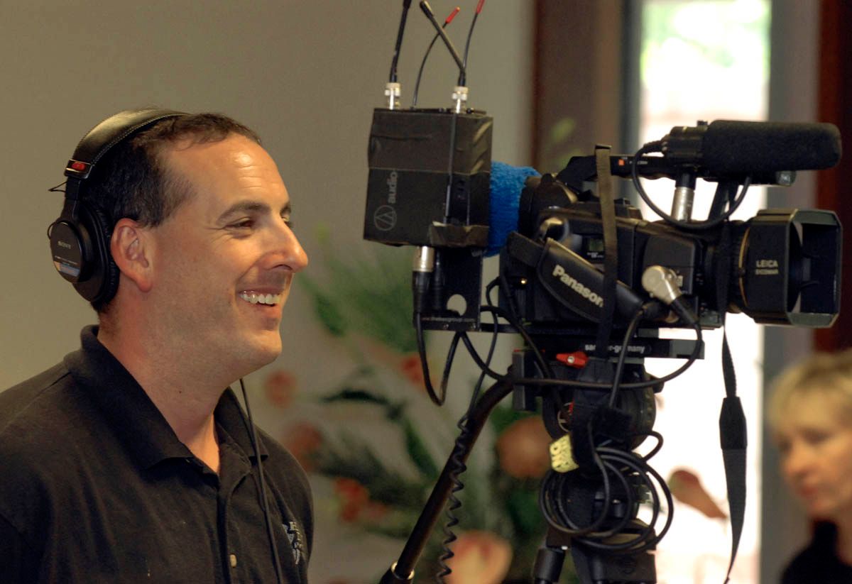 A man wearing headphones stands in front of a panasonic camera