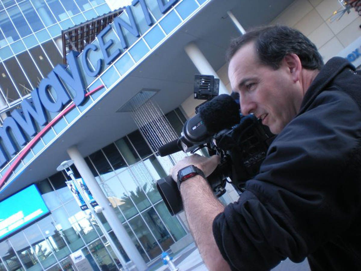 A man is holding a camera in front of a building that says invincible