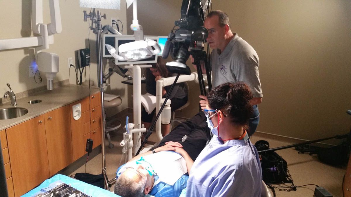 A man is taking a picture of a woman in a dental chair.