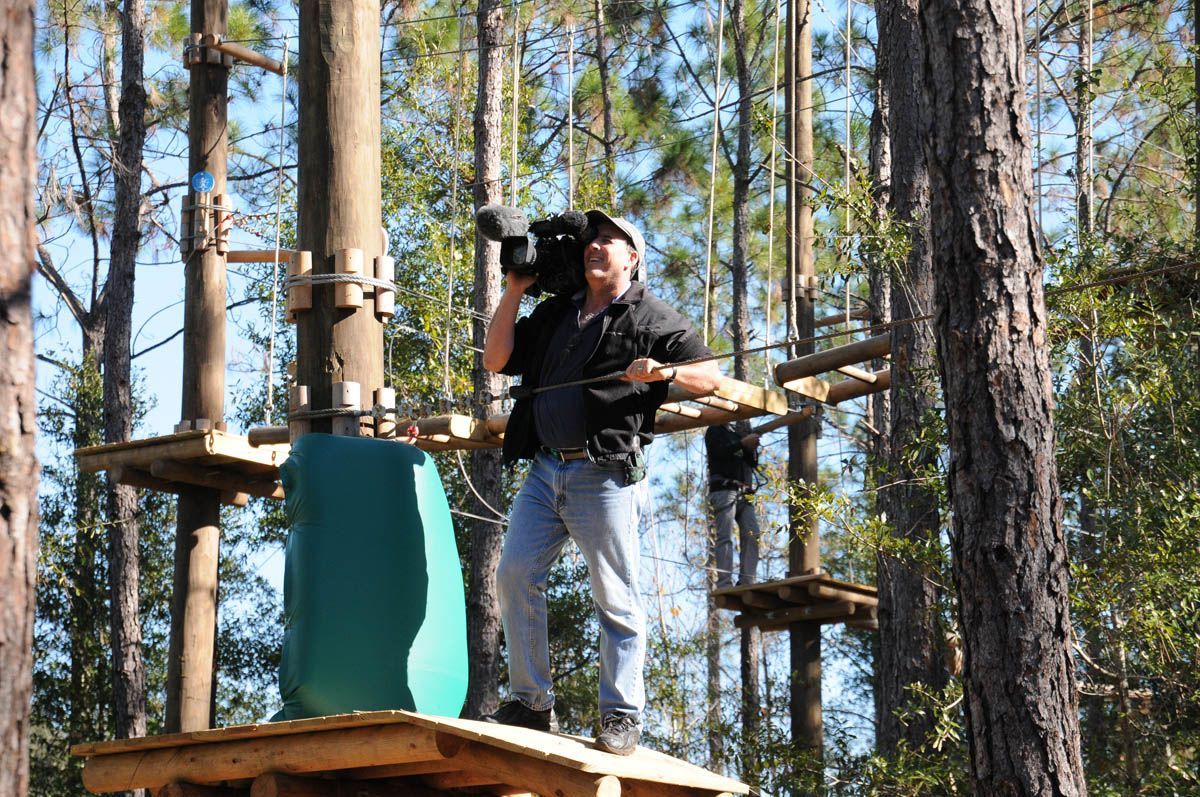 A man is standing on a platform in the woods holding a camera.