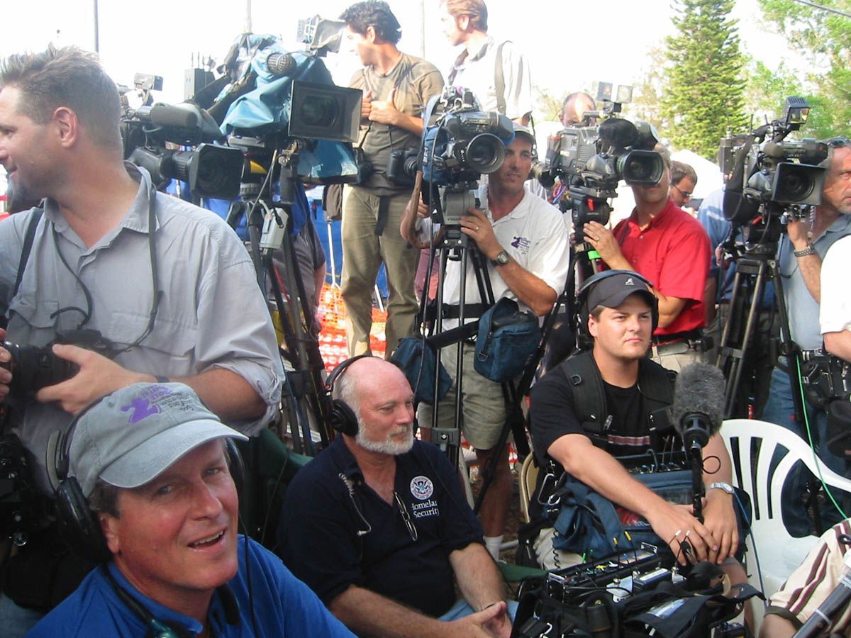 A group of men are sitting in front of cameras with one man wearing a hat that says u.s. army