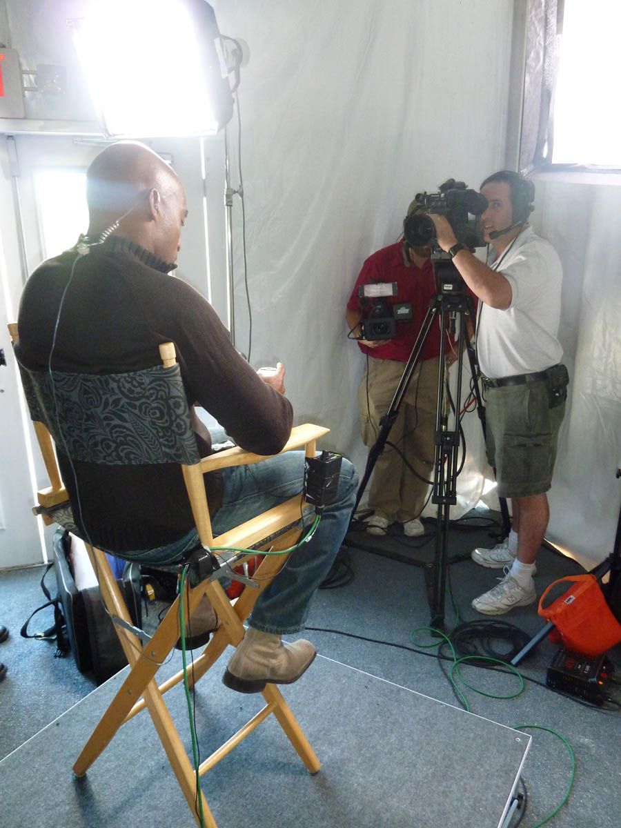 A man is sitting in a director 's chair in front of a camera
