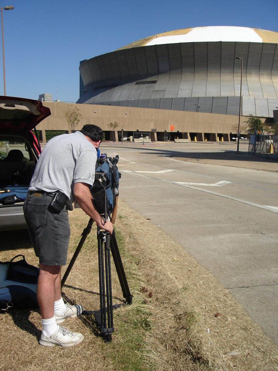 A man is setting up a camera on a tripod in front of a large building