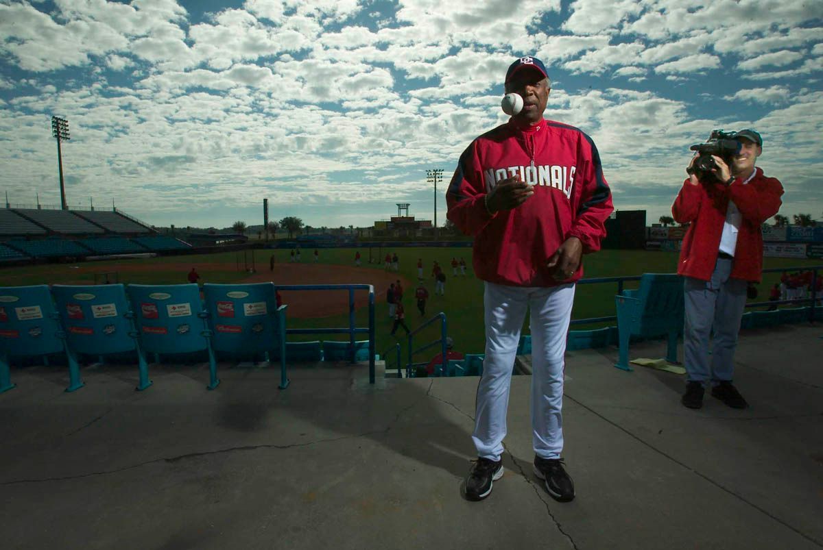 A man in a red jacket is standing on a baseball field holding a baseball.