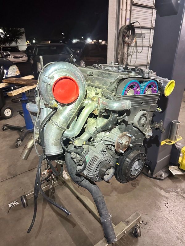Turbocharged engine on a stand, illuminated in a garage. Silver, red, and blue components.