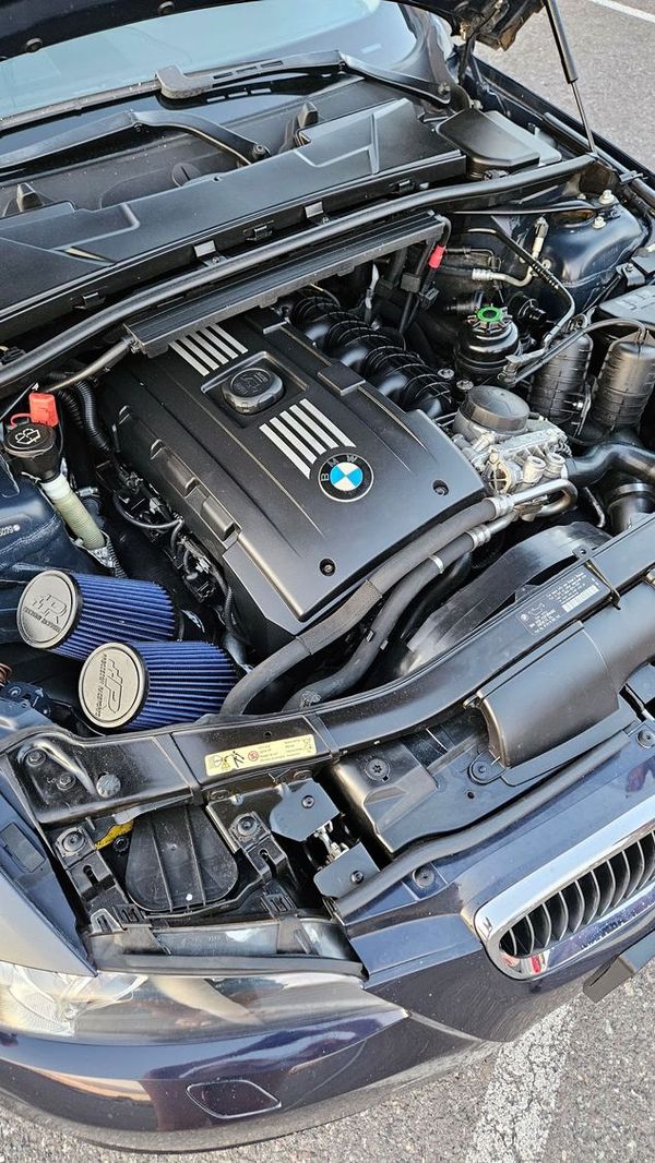 BMW car engine bay with black engine cover, blue air filters.
